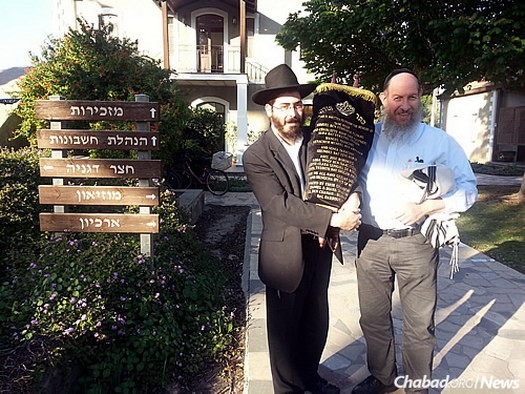 Joszef Jicchák Blau rabbi kezében az új tóratekerccsel Degánjában. Mellette Bentzion Chanowitz, a brooklyni Beis Yisroel Torah Gemach képviselője.
