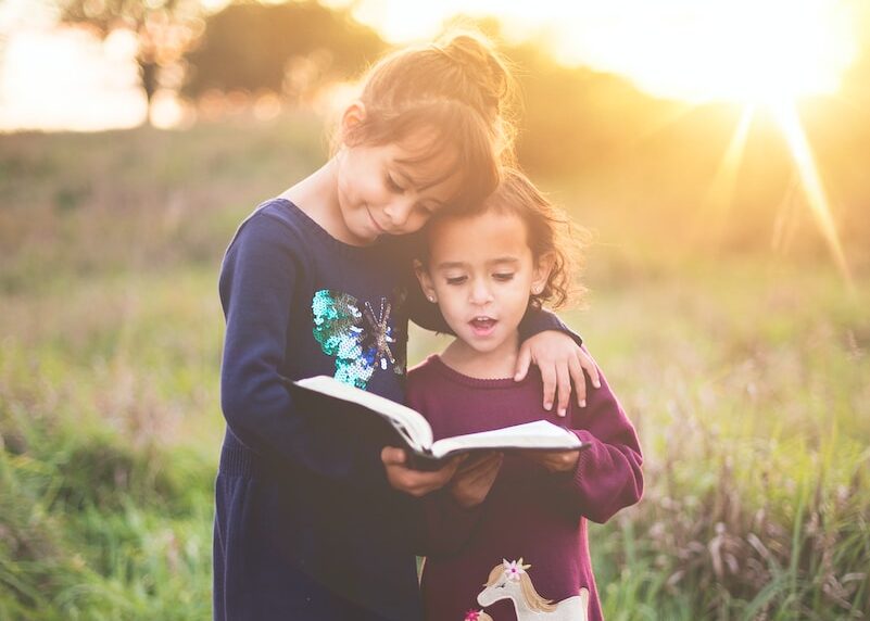 girl's left hand wrap around toddler while reading book during golden hour