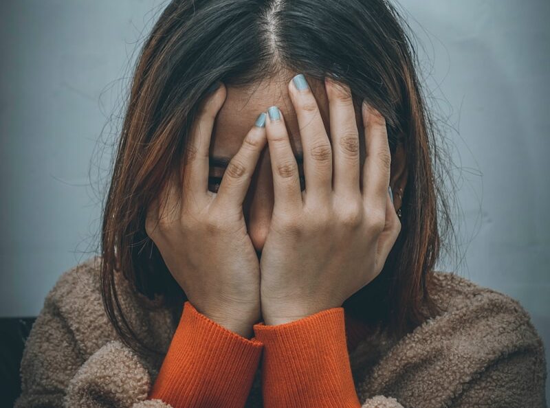 woman in brown sweater covering her face with her hand